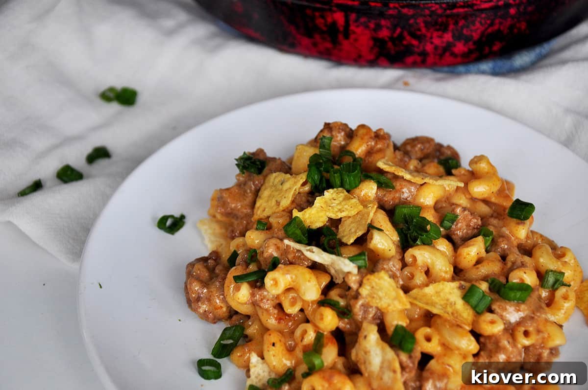A generous serving of Beefy Taco Mac and Cheese on a white plate, garnished with fresh toppings.
