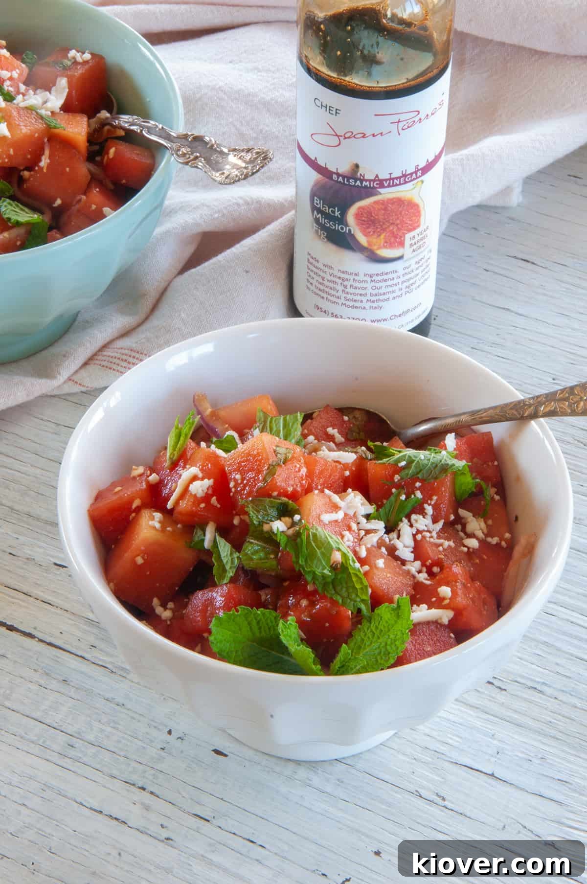 Bowl of watermelon feta salad and a jar of Black Mission Fig balsamic vinegar in the background.
