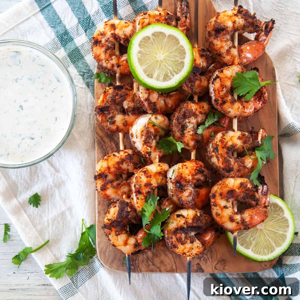 Perfect Grilled Blackened Shrimp Four blackened shrimp skewers on a wood cutting board with cilantro sprinkled on top, showcasing a perfect summer meal.