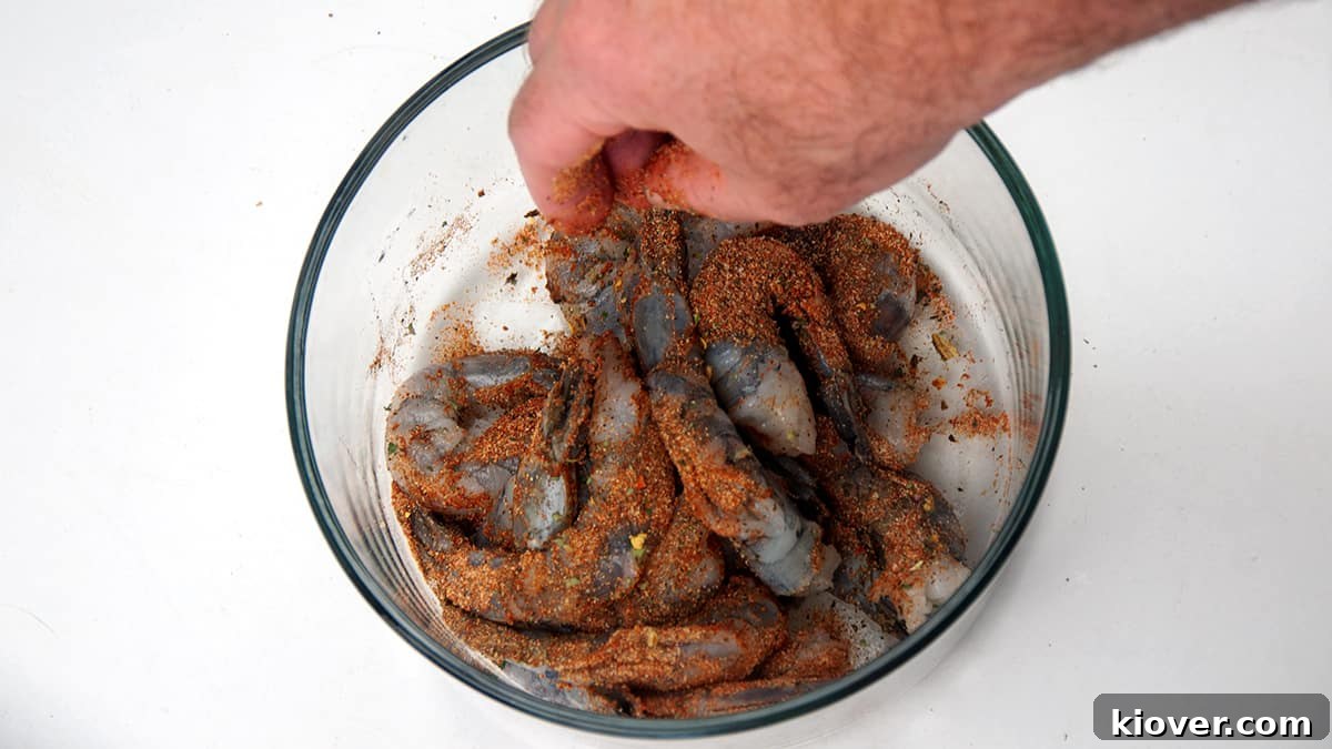 Coating Shrimp with Blackening Seasoning Hand in container spreading blackening spice over shrimp, ensuring even coating for maximum flavor.
