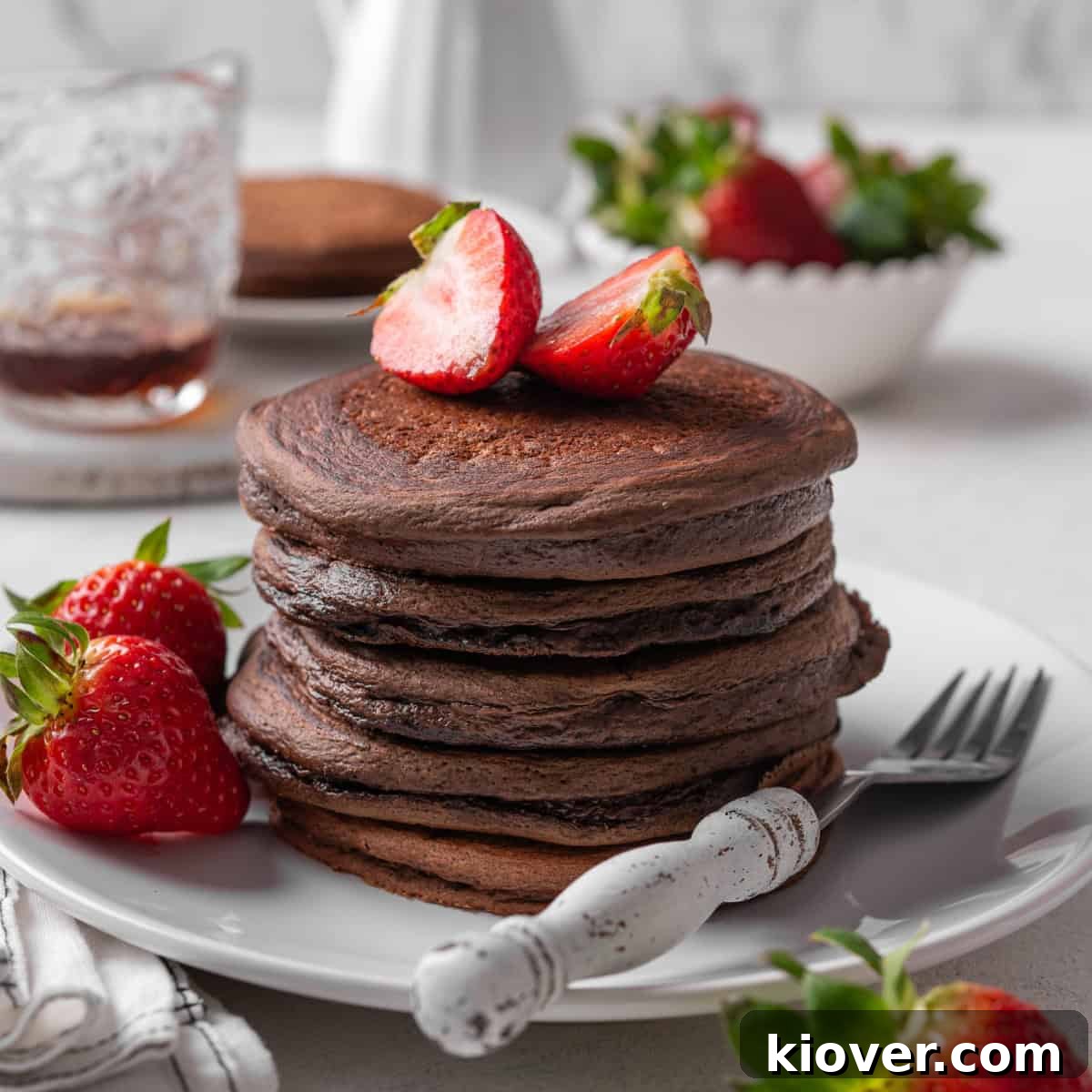 Decadent Chocolate Pancakes 2 A stack of fluffy chocolate pancakes garnished with fresh strawberries and a drizzle of maple syrup.