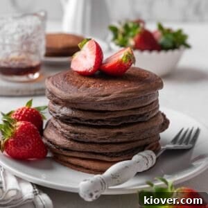 A beautiful stack of chocolate pancakes garnished with fresh strawberries.