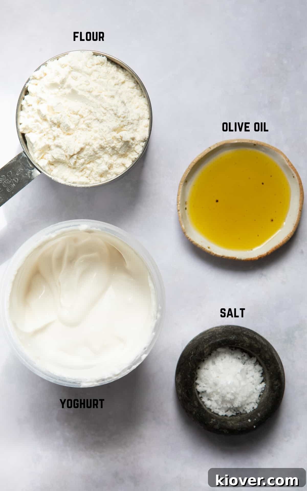 A collection of ingredients to make gluten-free naan bread including flour, yogurt, and olive oil, arranged neatly on a white surface.