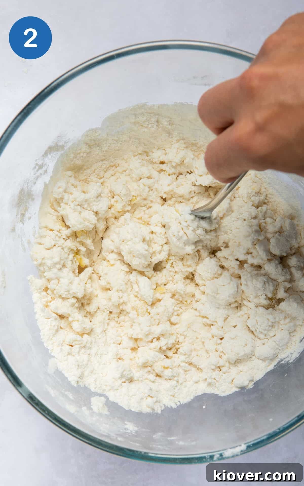 The naan dough ingredients being expertly mixed in a large bowl with a fork, starting to combine into a cohesive mass.