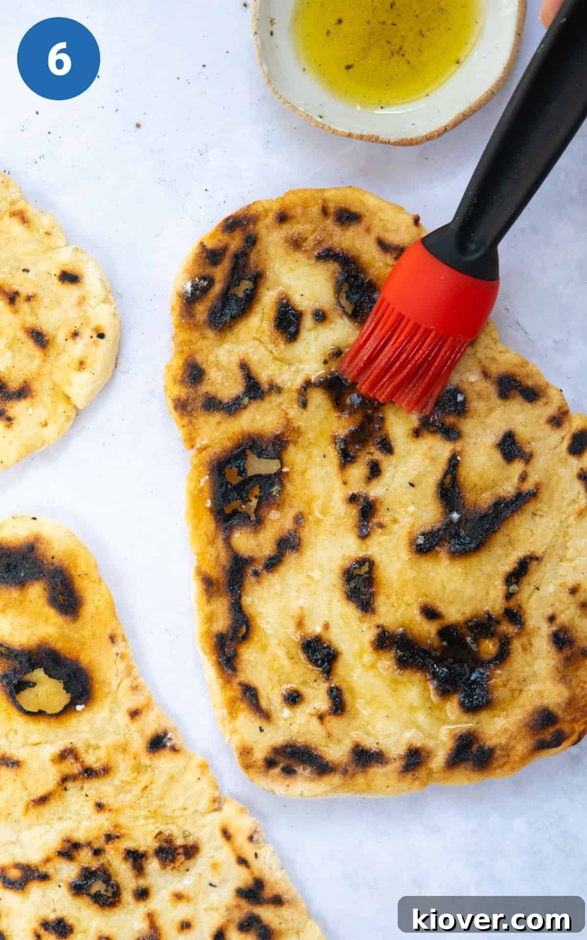 A freshly cooked gluten-free naan bread on a white background, being brushed with olive oil for added flavour and sheen.
