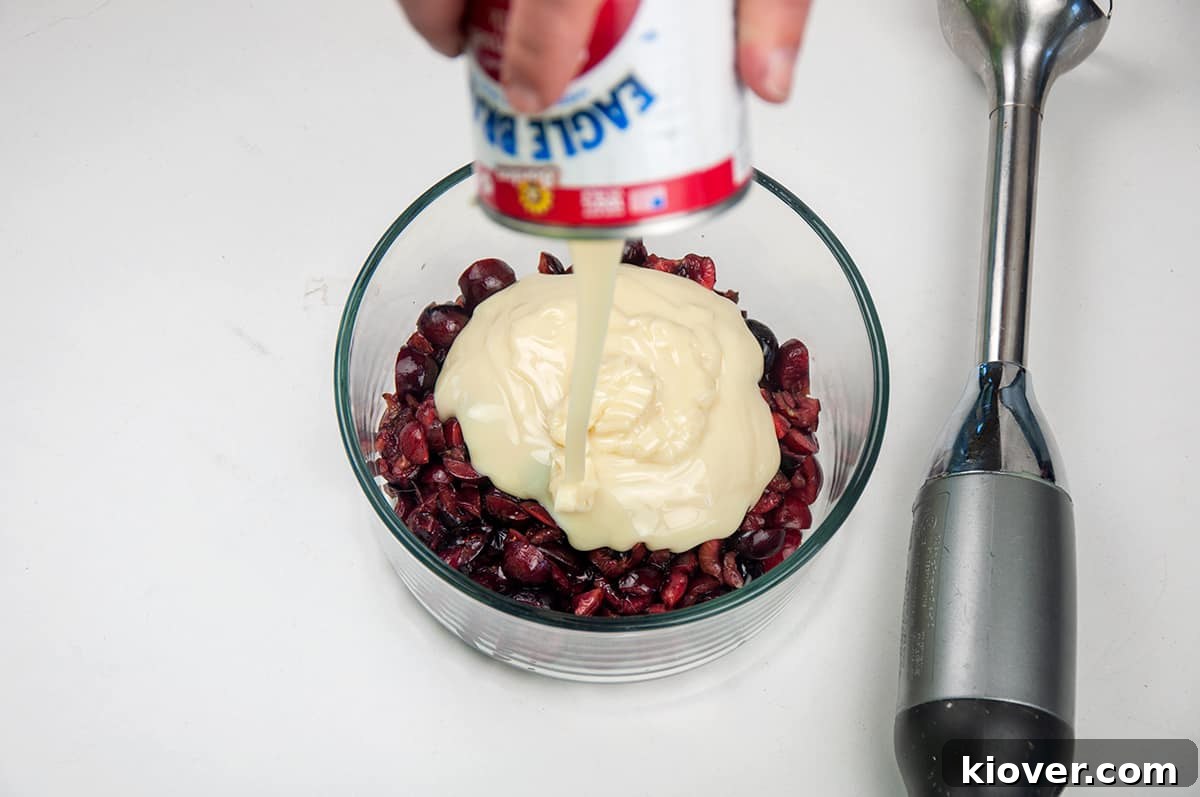 Pouring sweetened condensed milk into a bowl of chopped cherries.