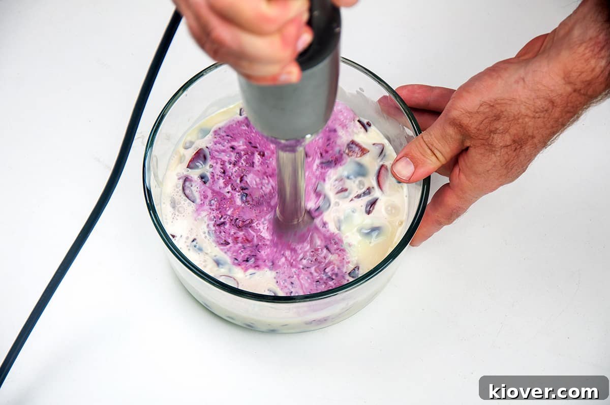 Cherries, heavy cream, and condensed milk being blended with an immersion blender.