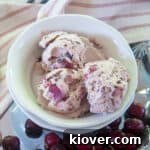 Three Scoops of No-Churn Black Cherry Ice cream in a bowl with fresh cherries to the side.