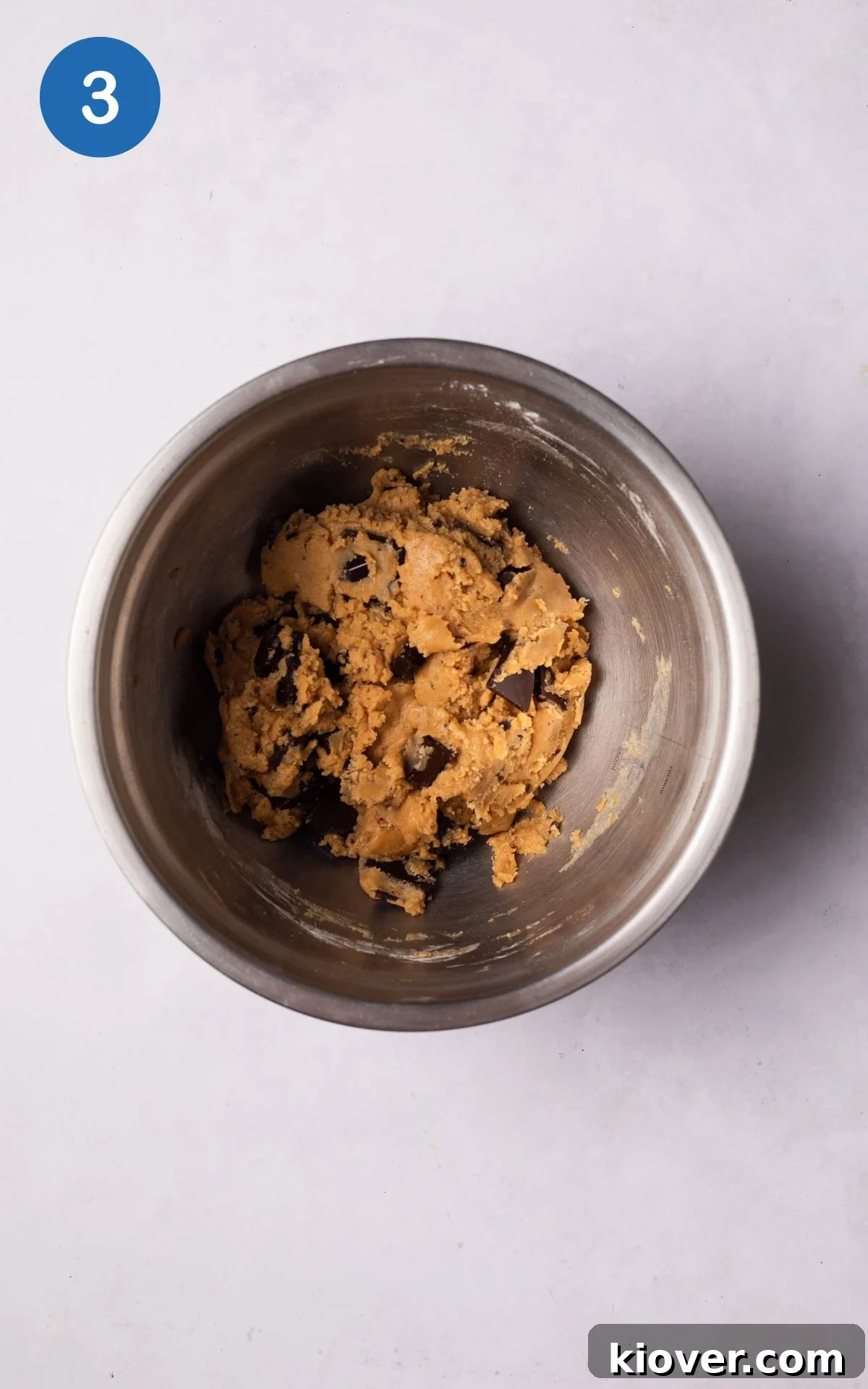 Dry ingredients, including flour and chopped chocolate, being added to the wet mixture in a large bowl, prior to mixing.