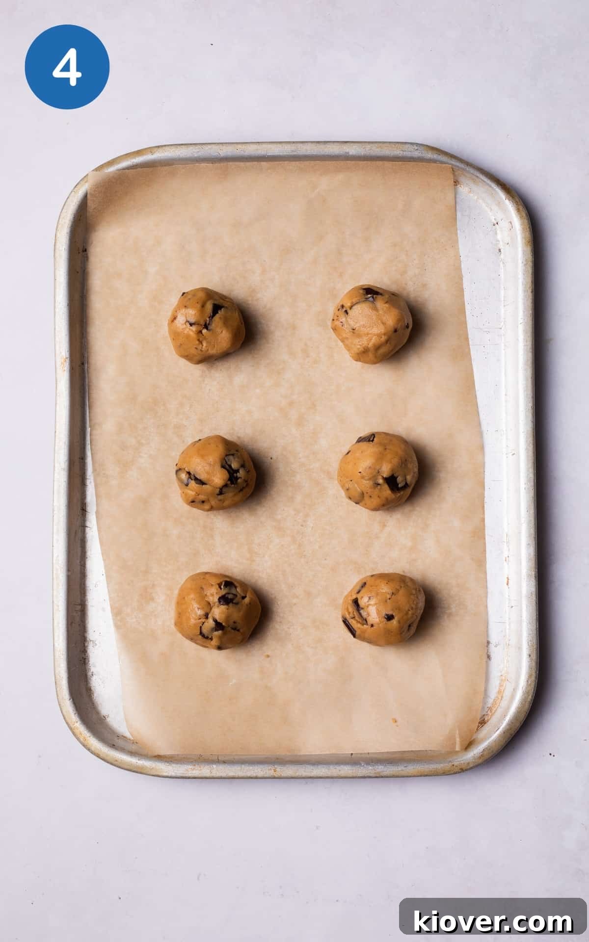 Six evenly rolled balls of vegan peanut butter cookie dough placed on a baking tray lined with parchment paper, ready for baking.