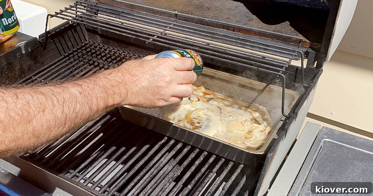 A hand pouring a can of amber ale beer into a baking pan already containing sautéed onions, garlic, and melted butter, ready for the bratwurst simmer.