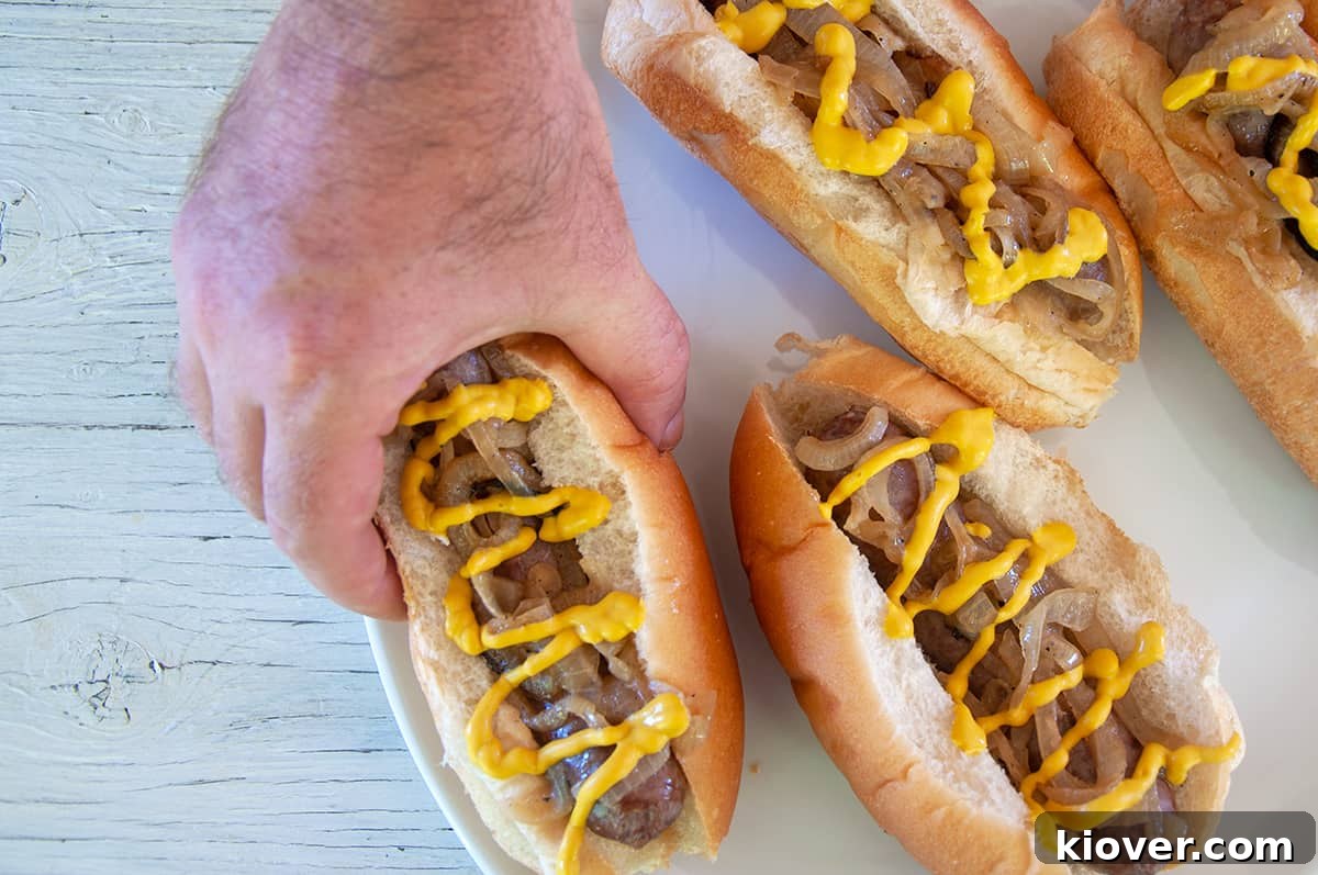 A hand reaching for one of four perfectly cooked beer brats served on a platter, ready to be enjoyed.