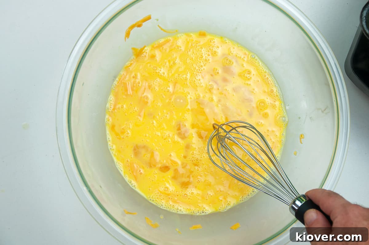 Eggs, milk, and cheese are vigorously whisked together in a large glass bowl, a necessary step for the frittata preparation.