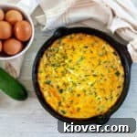 Cast iron skillet with Zucchini Frittata and whole eggs and a raw zucchini to the side.