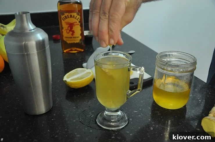Squeezing lemon into completed 'Hot Toddy for a Cold' cocktail. Fireball, honey, and lemon in background.