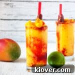 Two Mangonadas with Tamarind candy straws on a white table with a mango and lime.