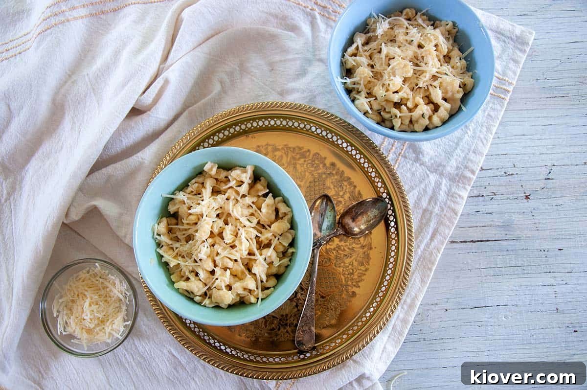 A beautifully presented bowl of butter-fried Spaetzle, garnished with fresh herbs, resting on a elegant gold platter alongside two serving spoons, ready to be shared.