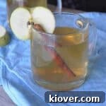 Apple Ginger Hot Toddy in irish coffee mug with cinnamon stick and apple slice.