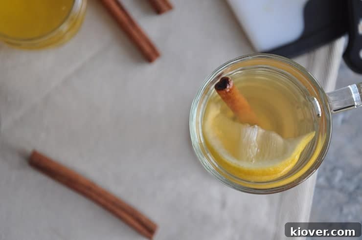Overhead shot of a Hot Toddy in a mug, garnished with a cinnamon stick, against a tablecloth background.