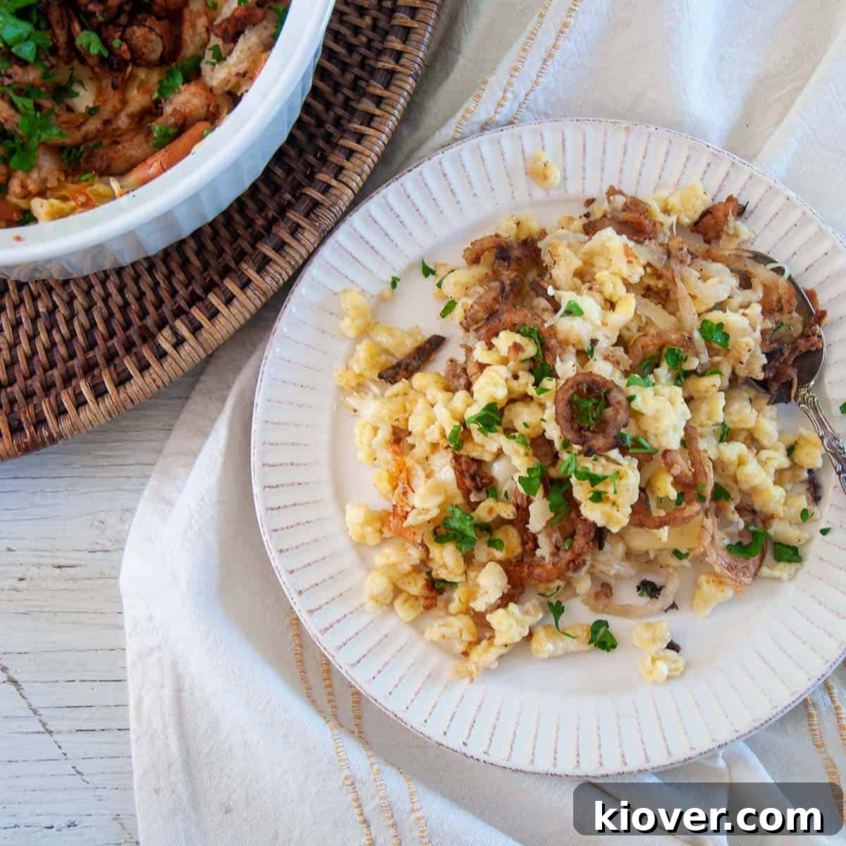 Käsespätzle German Käsespätzle dumplings on a white plate with a casserole dish full of it to the side.