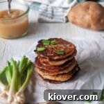 Crispy German Potato Pancakes on white paper with green onions and applesauce.