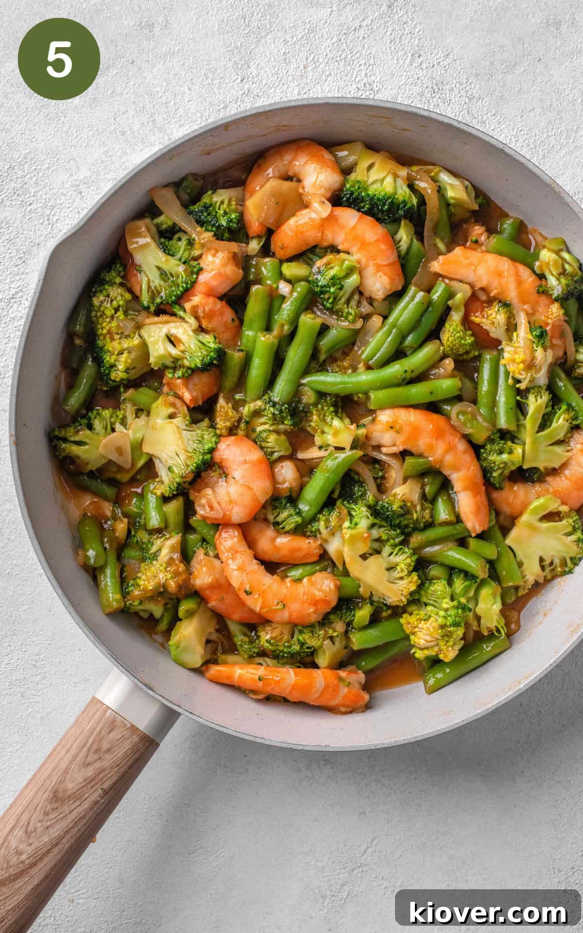 prawn stir fry cooked in a non stick frying pan, with thickened sauce coating the ingredients.