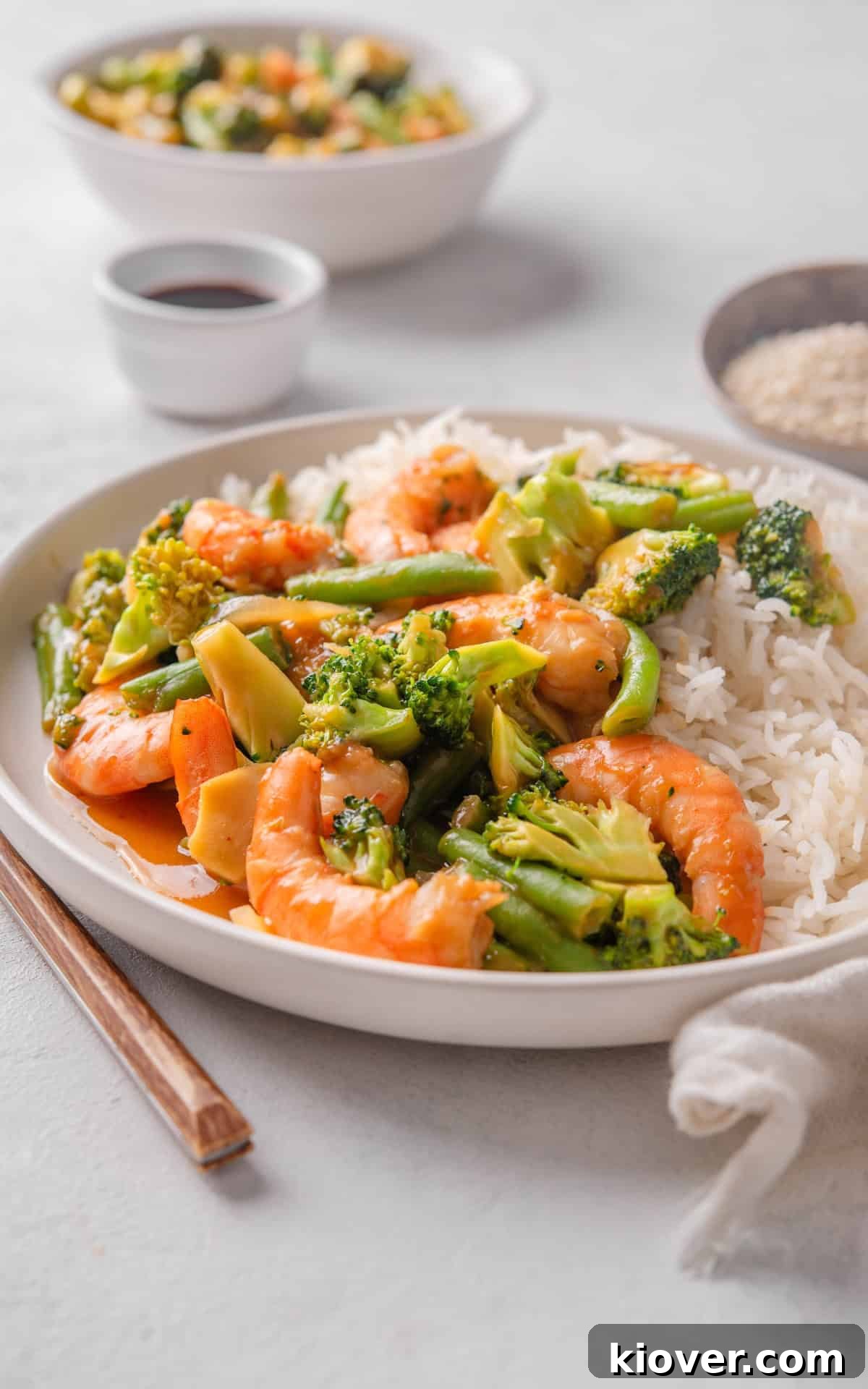 prawn stir fry served on a white plate with white rice and sesame seeds, ready to eat.