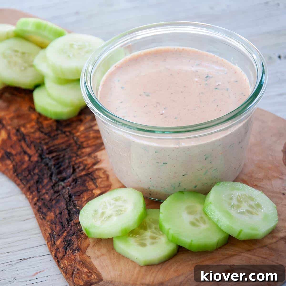 Creamy Chipotle Ranch Dressing and Dip in a glass jar, garnished with fresh herbs, on a rustic cutting board with sliced cucumbers nearby.