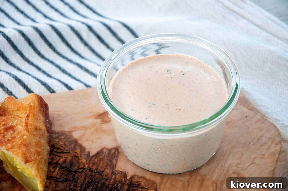 A glass jar of homemade Chipotle Ranch Dip on a wooden cutting board, with a fried pickle slice on the side.