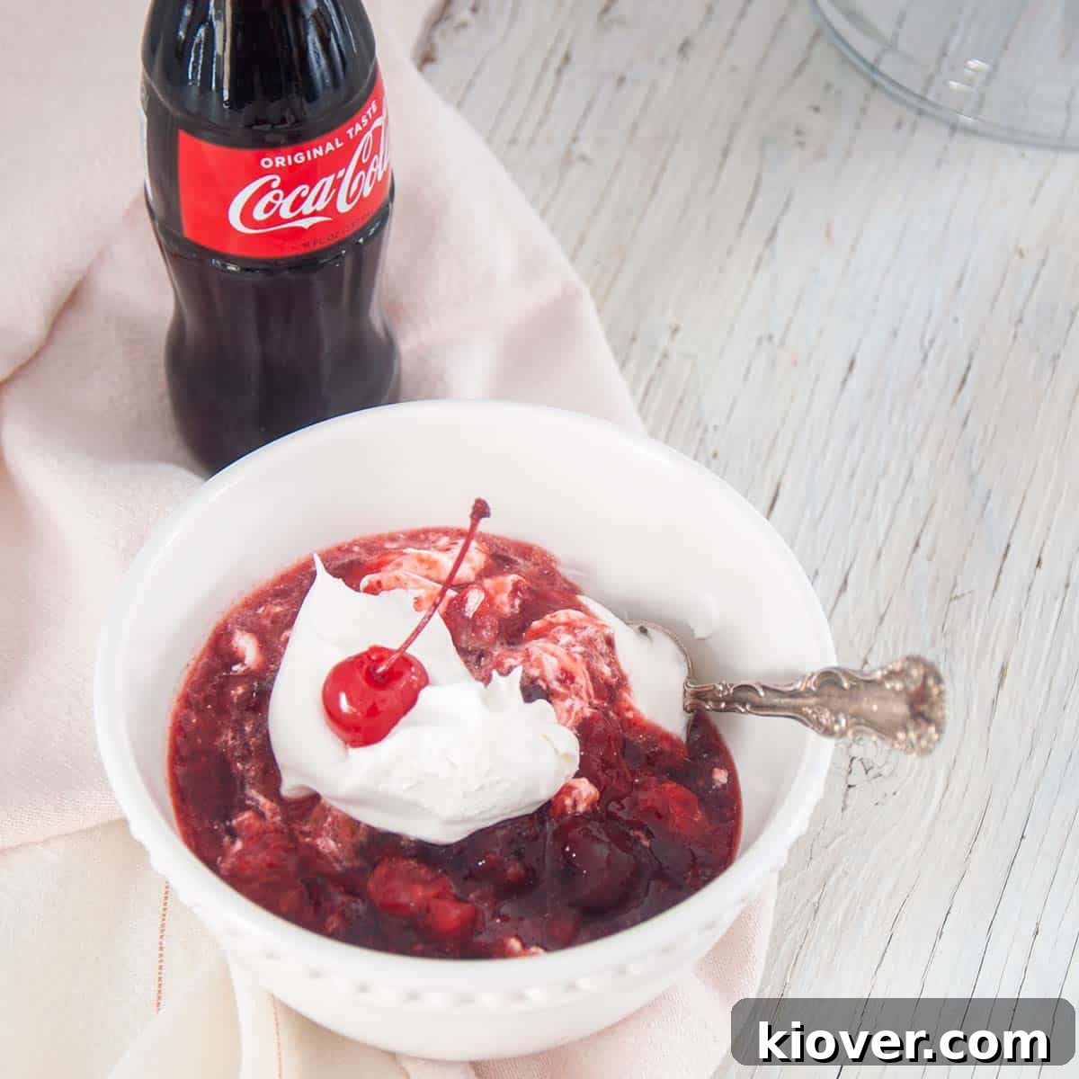 Individual Serving of Coke Salad A single serving of Coca-Cola Salad carefully dished into a crisp white bowl, generously topped with fluffy Cool Whip and a bright red maraschino cherry for garnish.