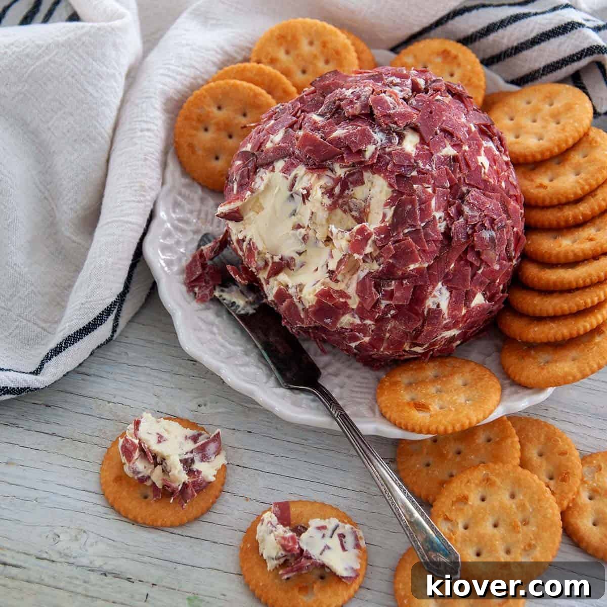 Classic Cheese Ball with Dried Beef Recipe A beautifully presented Cheese Ball with Dried Beef on a white plate, accompanied by two Ritz crackers topped with the irresistible spread.