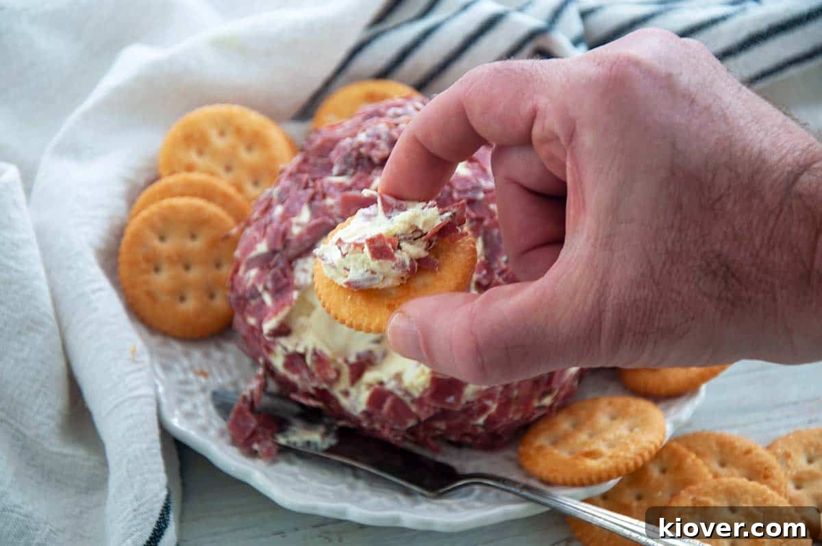 Artisan Dried Beef Cheese Ball 3 A hand holding a Ritz Cracker generously topped with a portion of the Dried Beef Cheeseball, ready for enjoyment.