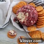 Cheeseball with dried beef on a white plate and two Ritz crackers with the dip on it.