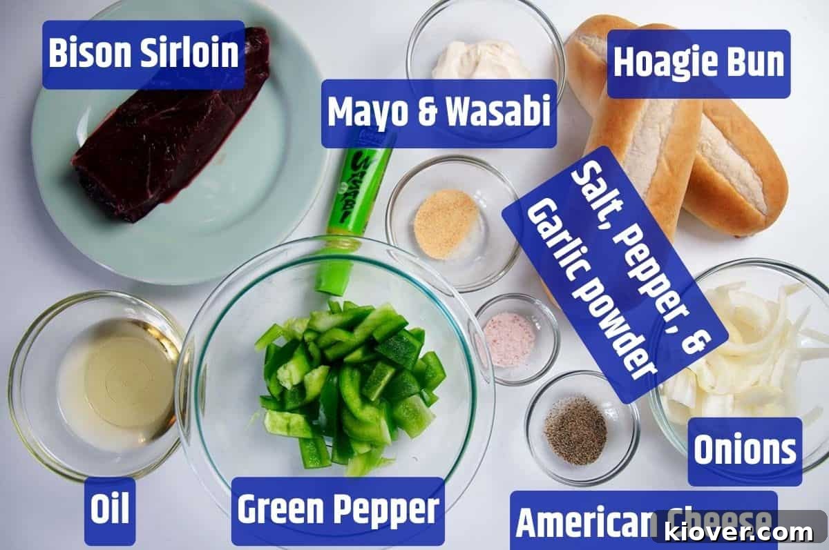A vibrant flat lay of ingredients for Bison Philly Cheesesteak, including bison sirloin, hoagie buns, fresh onion and green pepper, slices of American cheese, spices, and a small bowl of wasabi mayonnaise.