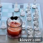 Manhattan cocktail in a lowball glass and one block of ice. There are two cherries garnishing this drink.