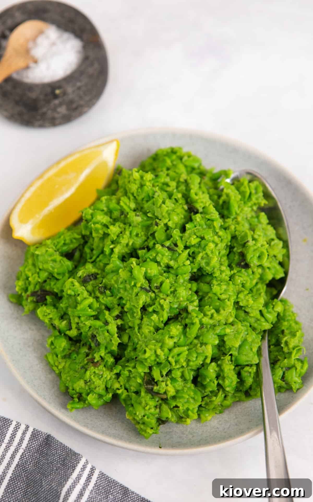 A serving of healthy mashed peas garnished with a lemon slice on a white plate.