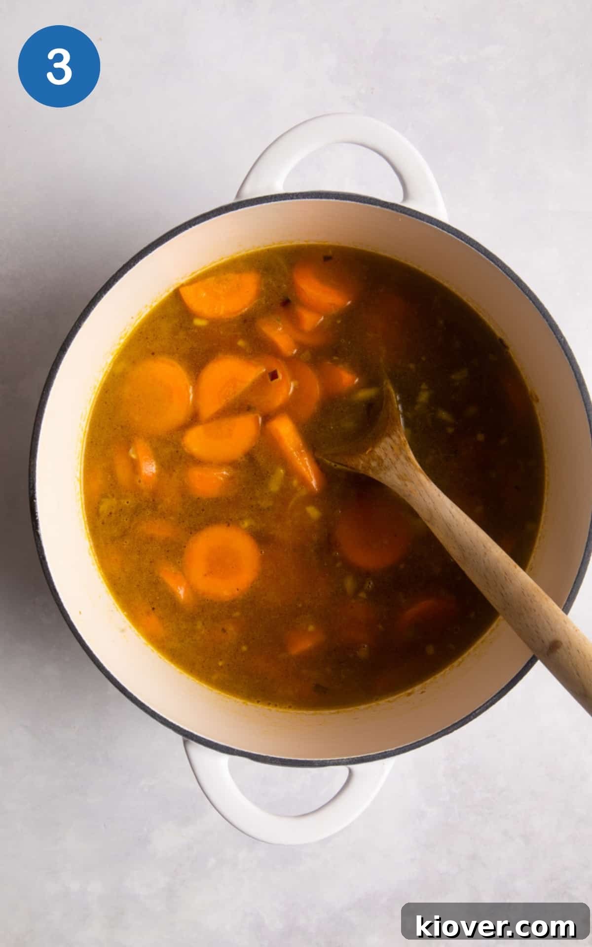 Simmering the carrot and coriander soup in a white pot.