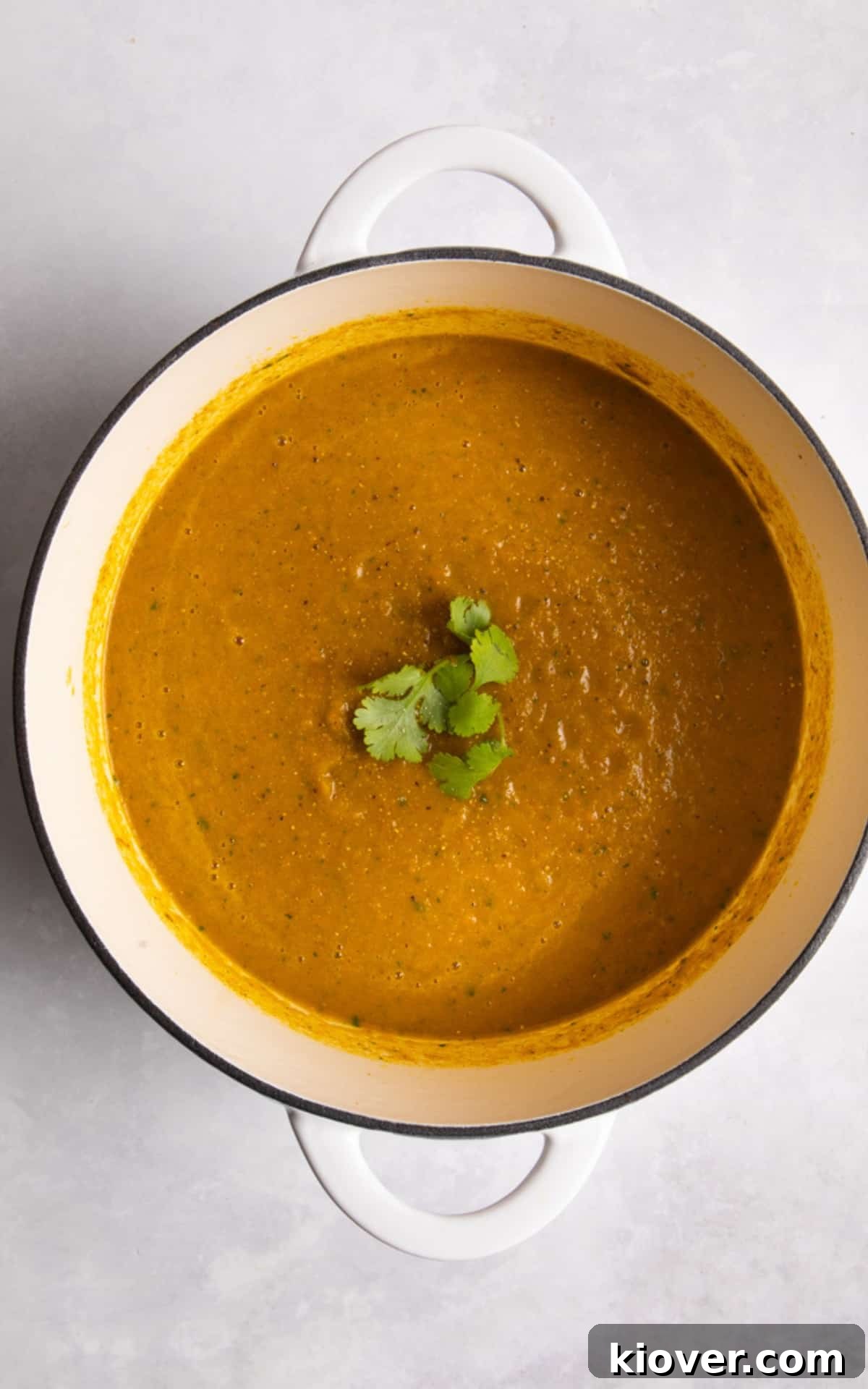 Blended carrot and coriander soup served in a white pot with fresh coriander on top.