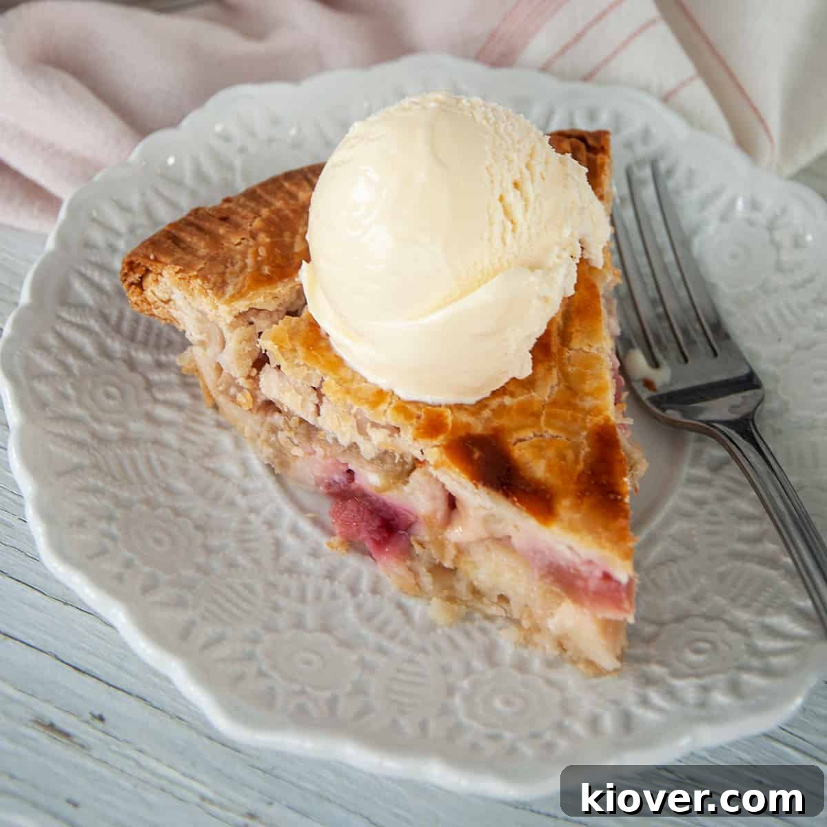 A delicious slice of homemade rhubarb pie on a white plate, showcasing its golden crust and vibrant filling.