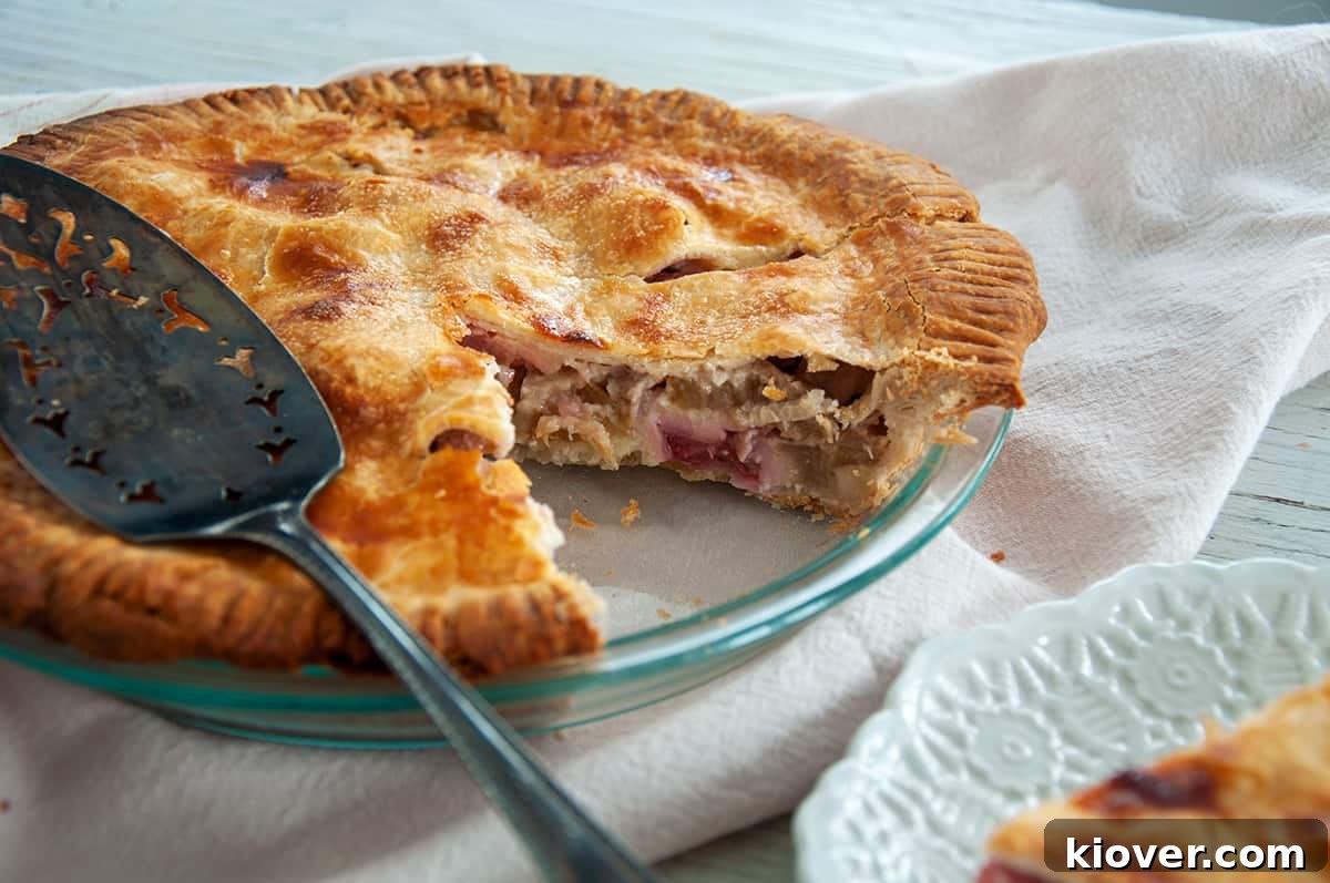 A whole rhubarb pie in a glass pie dish, with one slice removed to show the vibrant filling.