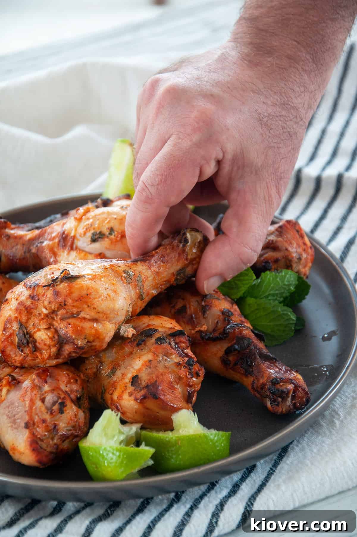 A hand reaching in to pick up a single grilled chicken leg from a mouth-watering stack of beautifully cooked chicken legs, ready to be enjoyed.