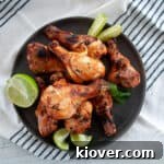 Several grilled chicken legs on a dark plate with mint and lime to the side.
