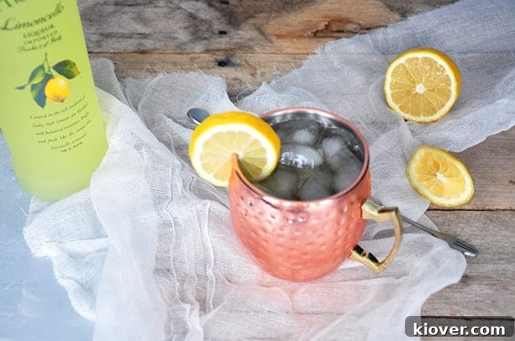 An overhead shot of a finished Limoncello and Lavender Moscow Mule in a gleaming copper mug, resting on a wooden table. A fresh lemon slice and lavender sprig serve as an elegant garnish.