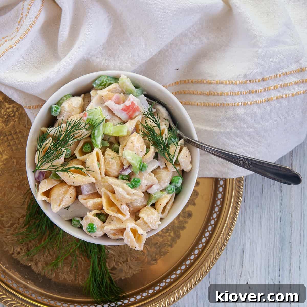 Crab Pasta Salad Crab pasta salad in a white bowl on a gold platter.