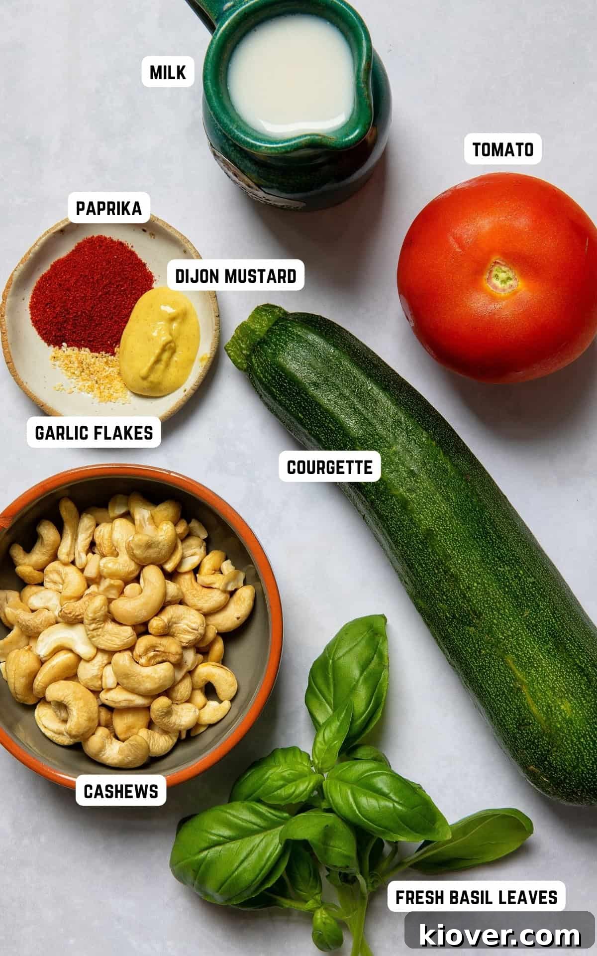 Fresh ingredients laid out on a kitchen surface: courgettes, tomatoes, basil, cashews, and spices ready for making the salad.