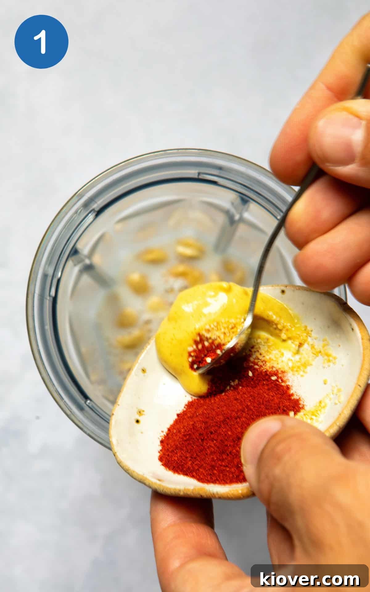 Adding Dijon mustard and various spices to a bowl, preparing the creamy cashew sauce.