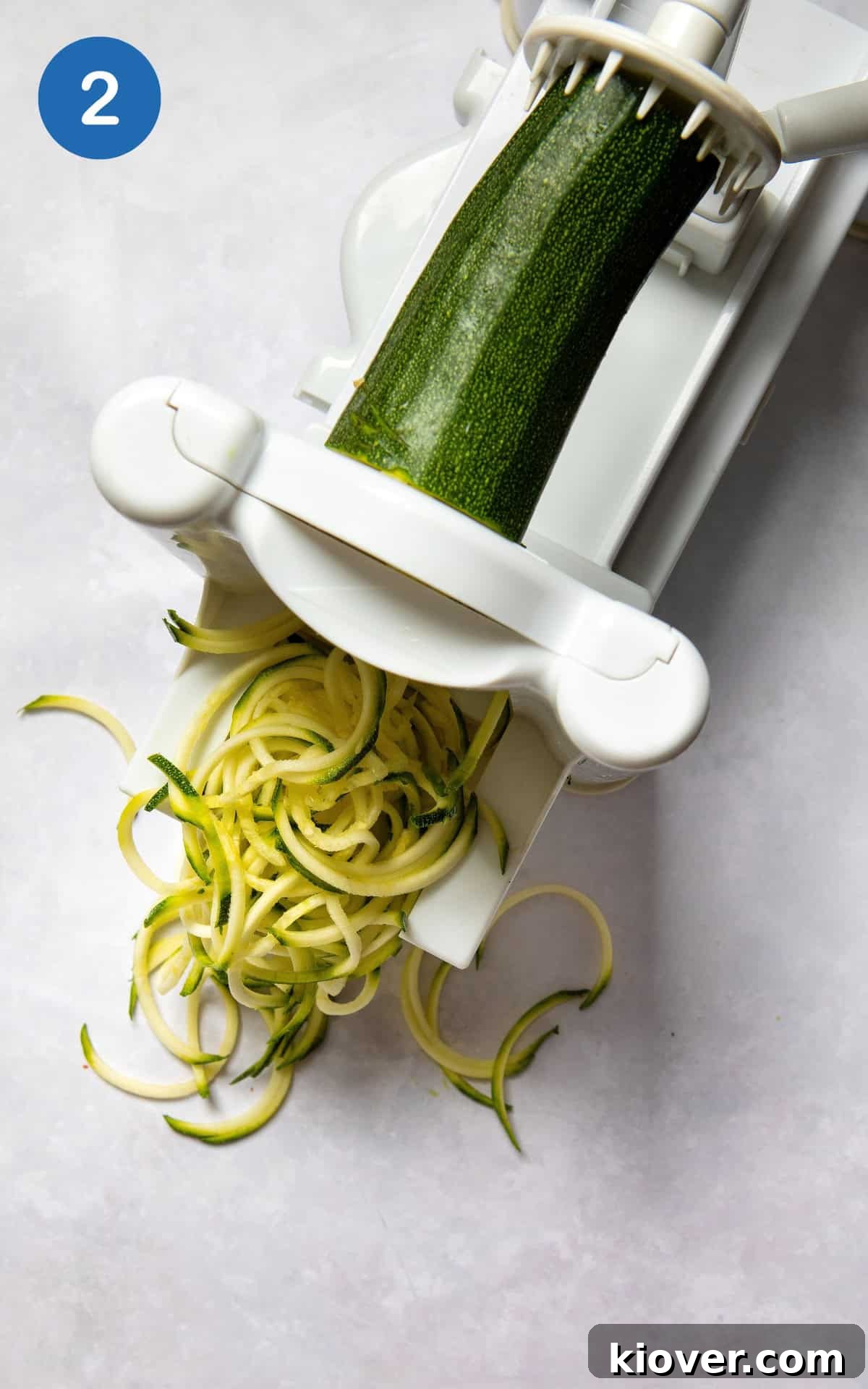 A spiralizer in action, creating delicate courgette noodles (zoodles) from a fresh courgette.