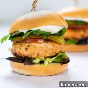 Salmon burger with bun and fresh lettuce on a white background.