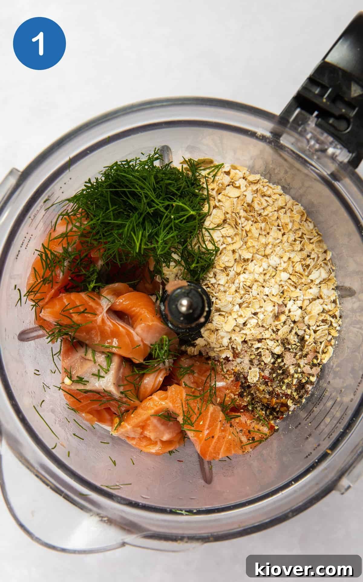 Ultimate Salmon Burgers 4 Ingredients for salmon burgers being combined in a food processor on a white surface.