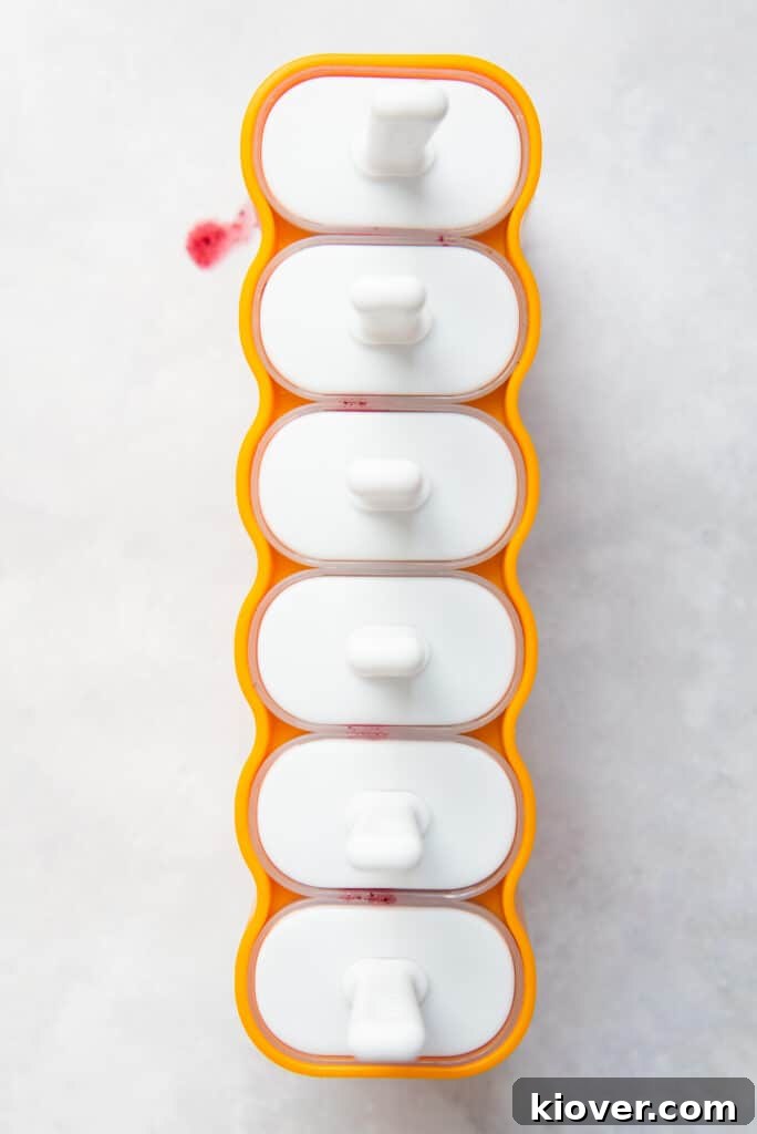 Multiple ice lolly molds filled with blueberry mixture, ready to be placed in the freezer.